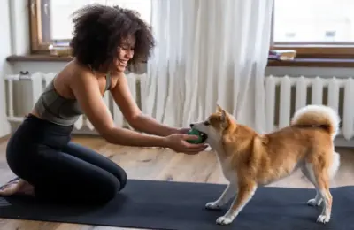 A joyful woman plays with her Shiba Inu dog indoors on a yoga mat, showcasing a warm and cozy home atmosphere.